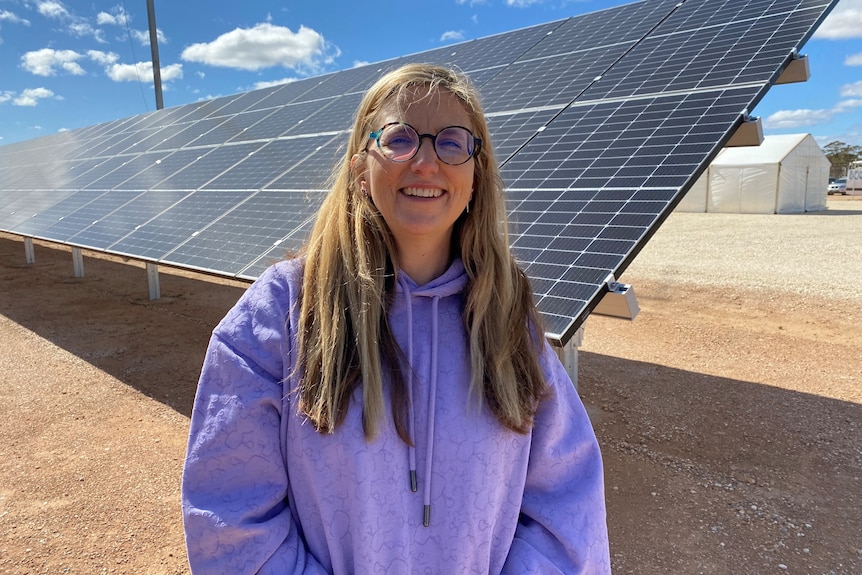 A woman in a purple jumper standing in front of a solar panel. 