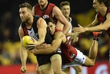 An AFL player holding a football, being tackled from behind by another player.