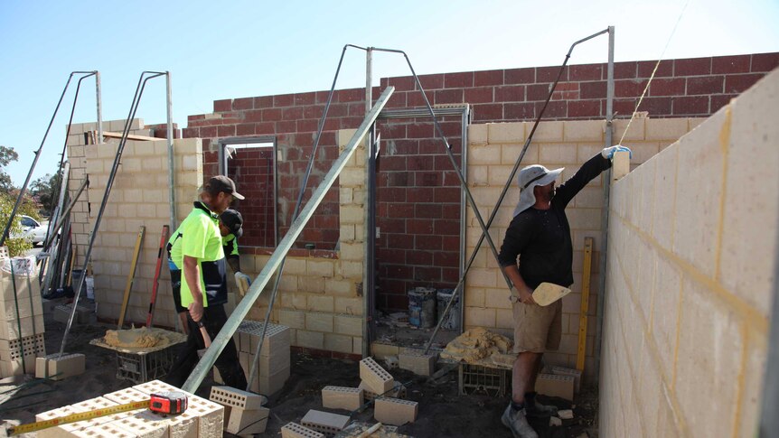 Three men working on house building site, laying brick walls