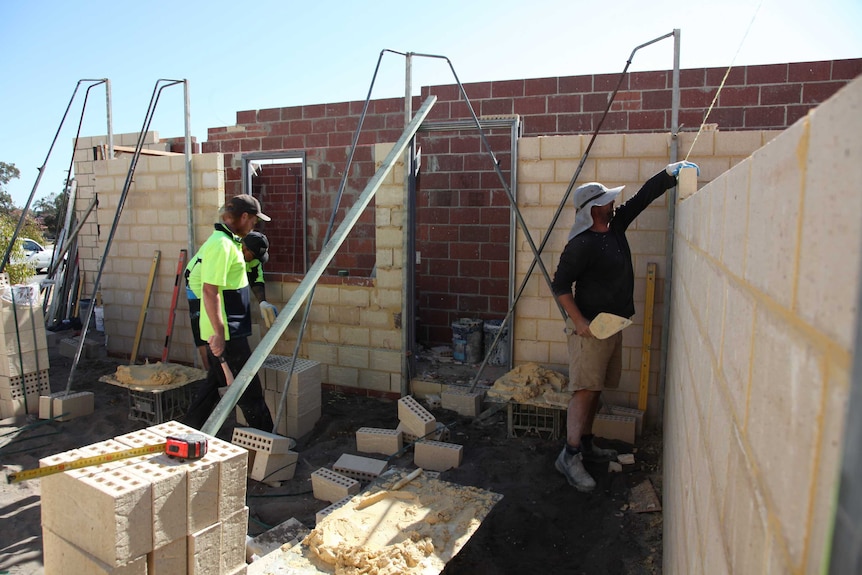Three men working on house building site, laying brick walls