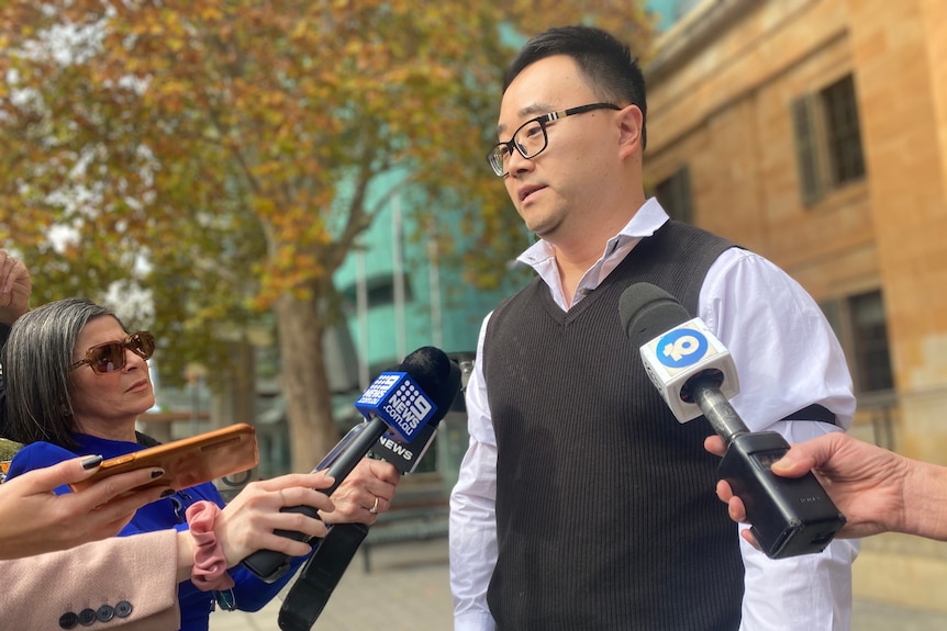 A man speaks into media microphones in front of a court building