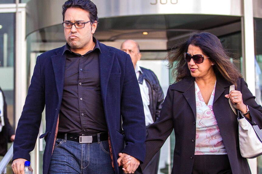 A man and a woman hold hands after walking out of a revolving door.