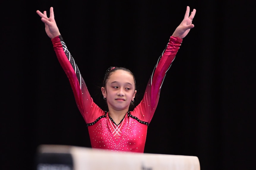 Trinity de Lance holds her arms above her to signal the end of her beam routine and looks to the side.