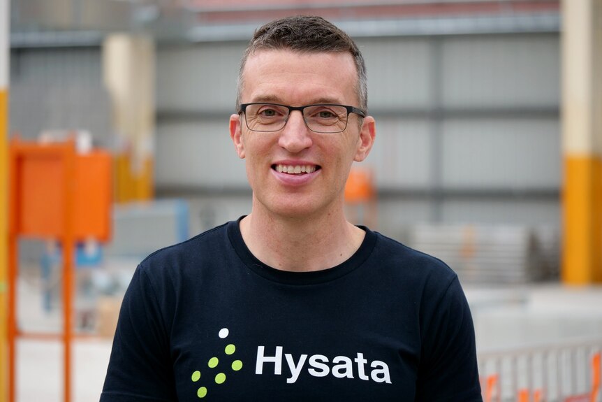 A man wearing glasses and a T-shirt with the word 'Hysata' on it, smiles for a photo.