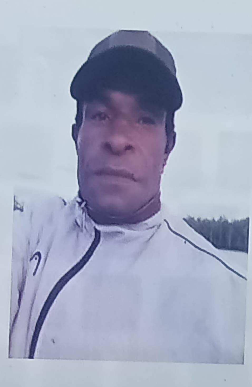 A man in a white jacket, black hat, looks at the camera.