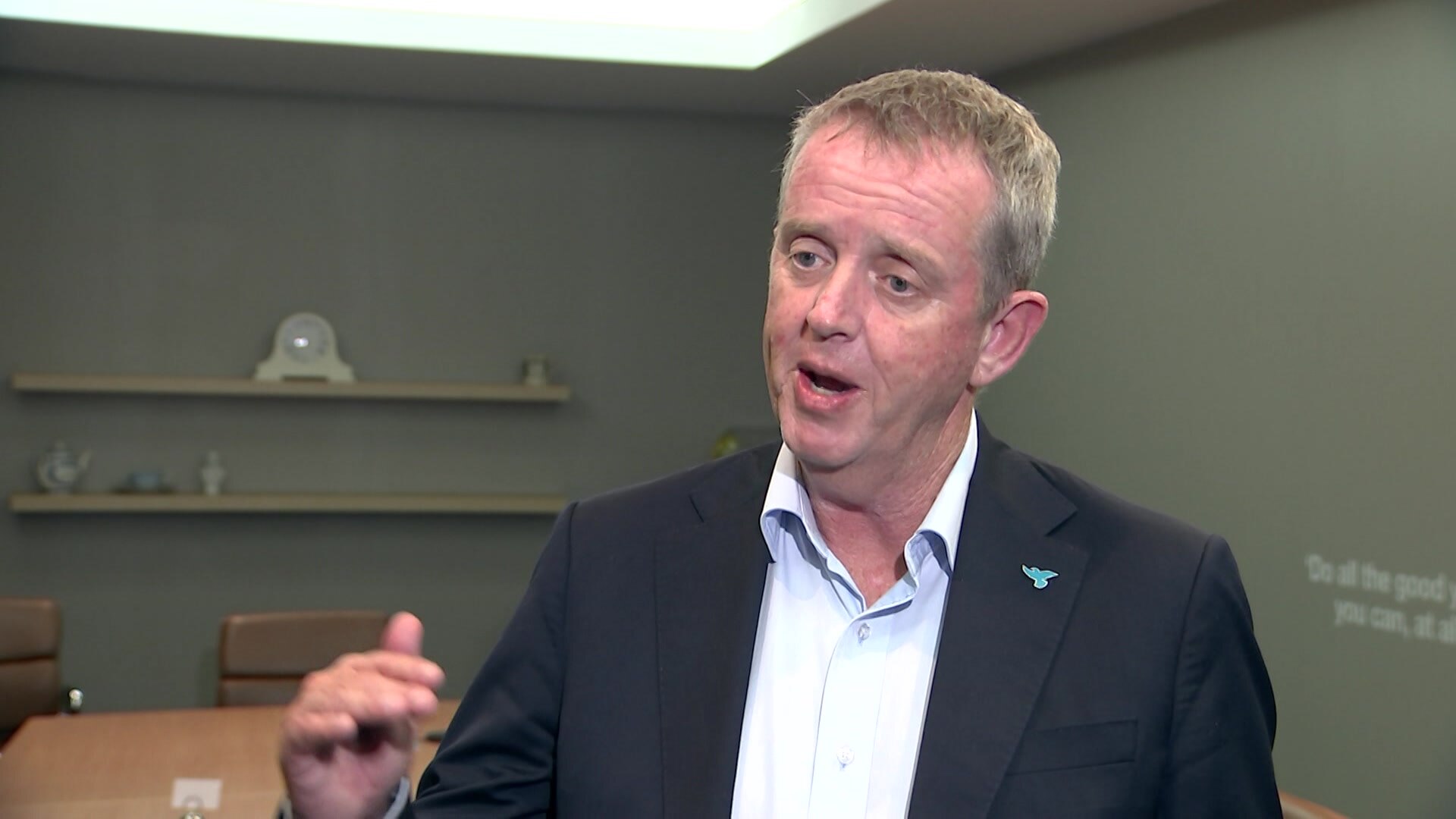 A man talks to the camera in an office meeting room.