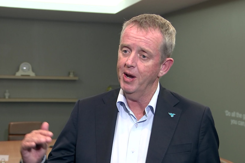 A man talks to the camera in an office meeting room.