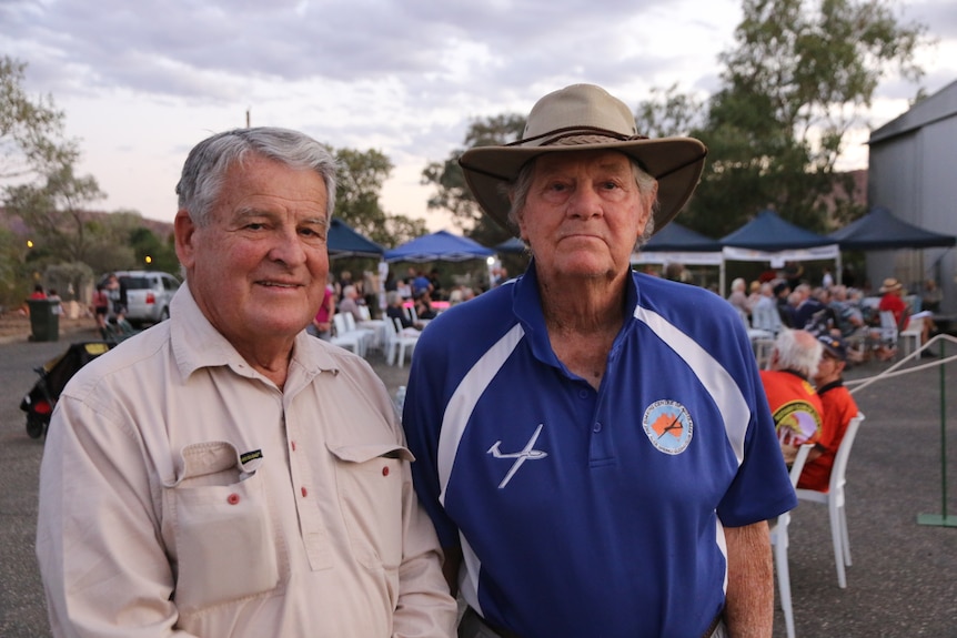 in the middle of two older men.  The man on the left wears a shirt and the man on the right wears a blue polo shirt and hat