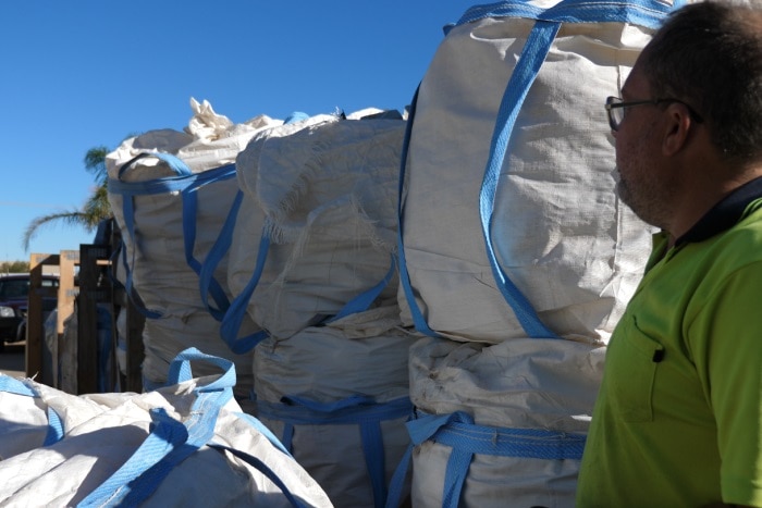 Michael Barker looking at large, white plastic bags which sit outside, they are full.