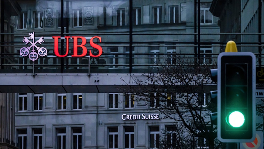 A grey European-style building sporting the logos of UBS and Credit Suisse, with a green traffic light to the right of it.