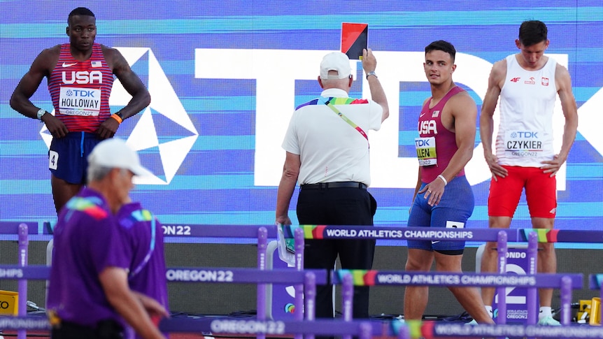 Devon Allen walks off as a judge shows him a coloured card at the start line of a hurdles race.