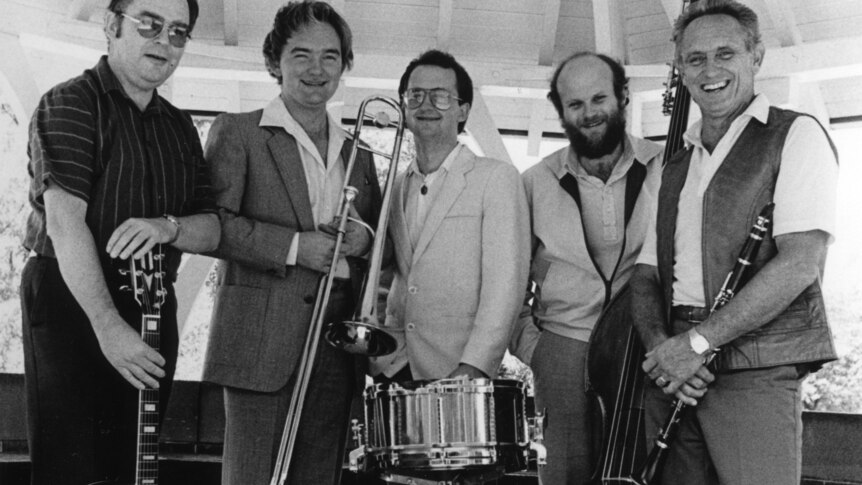 Five musicians in relaxed pose in outdoor band rotunda with (L-R) guitar, trombone, snare drum, double bass and clarinet