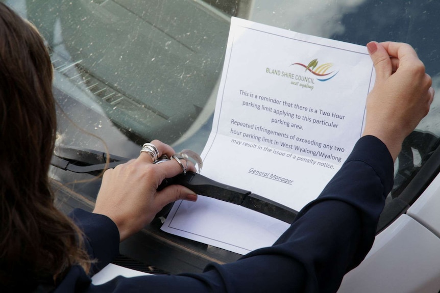 A woman pulls a parking warning from the windscreen of a white car