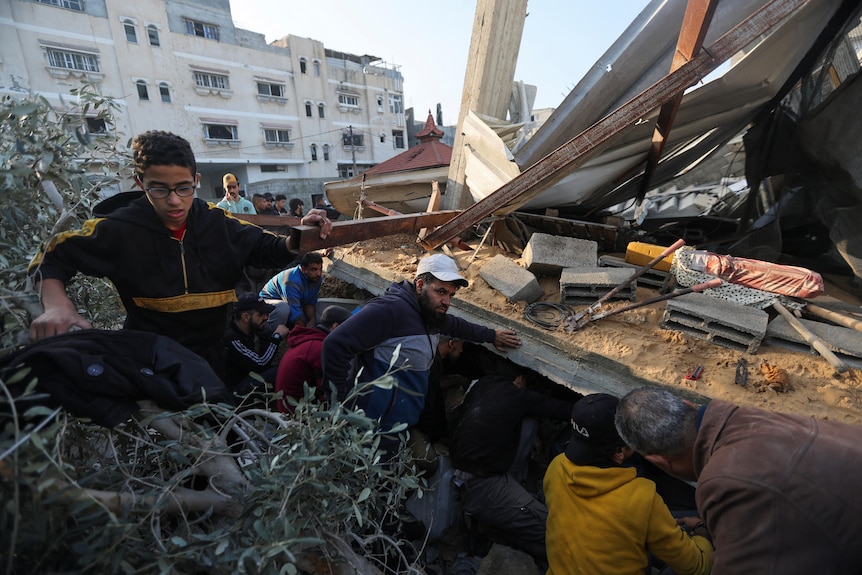 people crowd around a destroyed house trying to rescue people