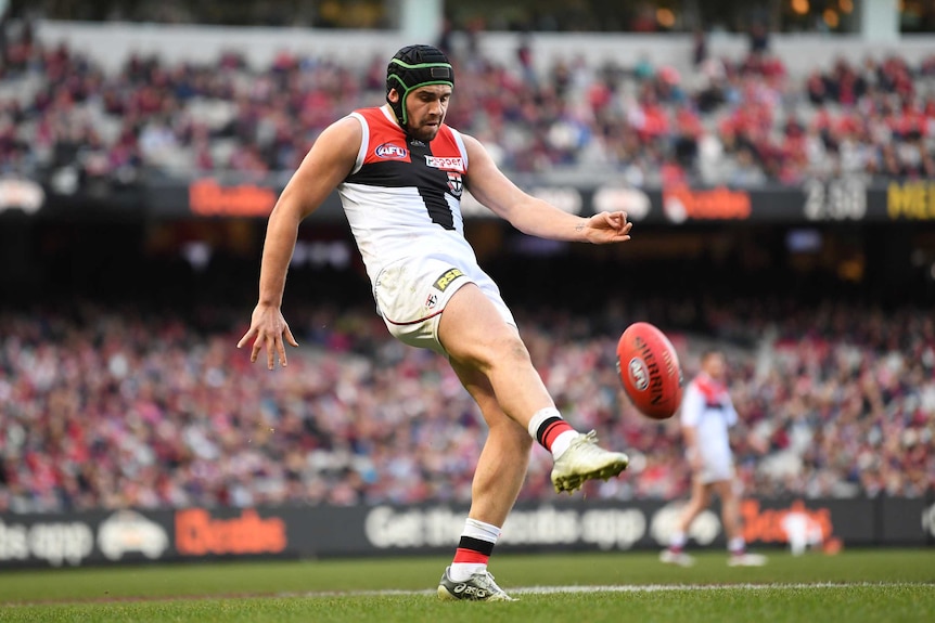 An AFL forward wearing protective headgear kicks through the ball at the MCG.