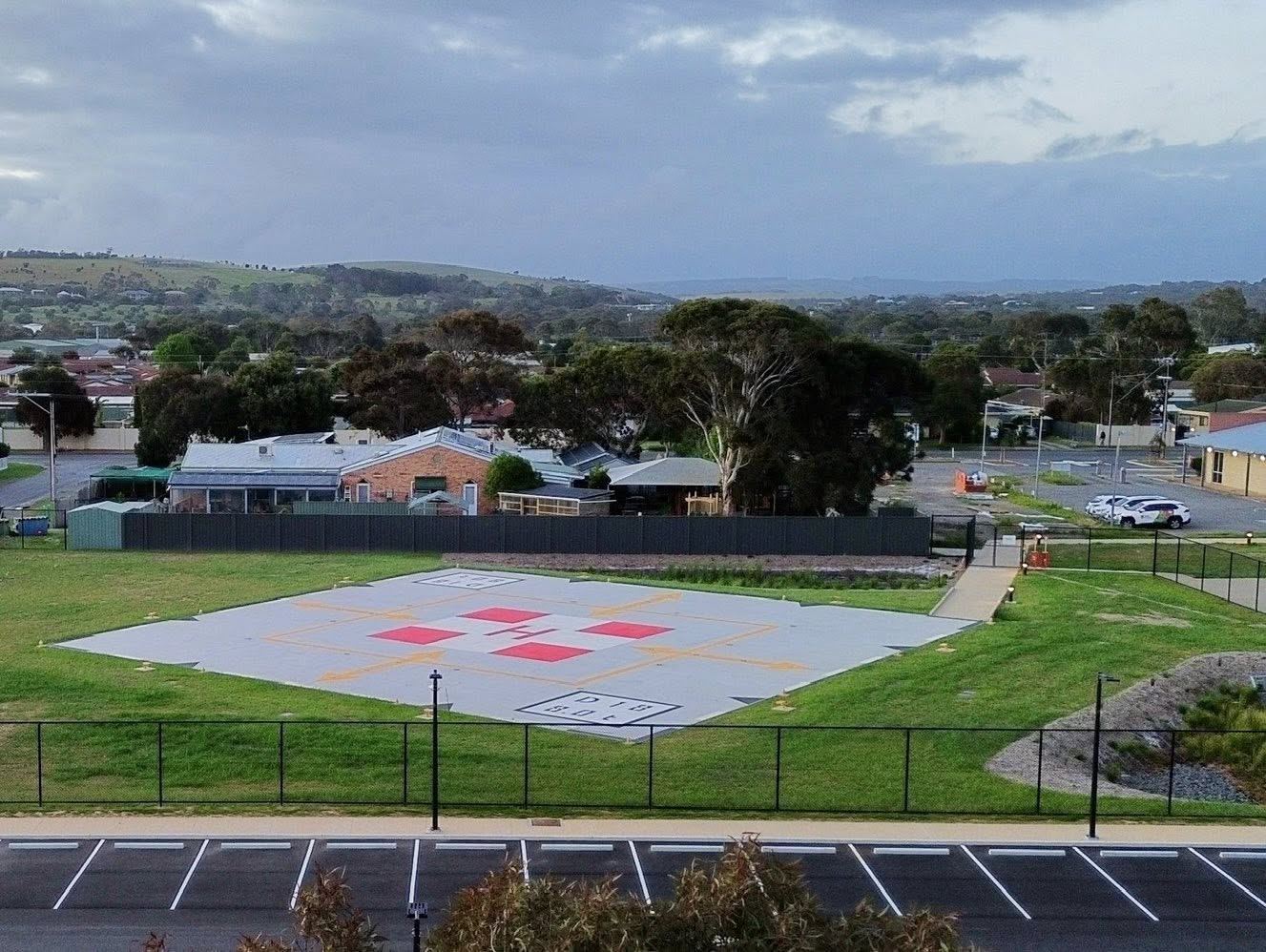 An elevated view shows a helipad located next to a car park and buildings.