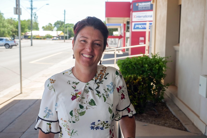 A woman smiles at a camera in a floral dress.