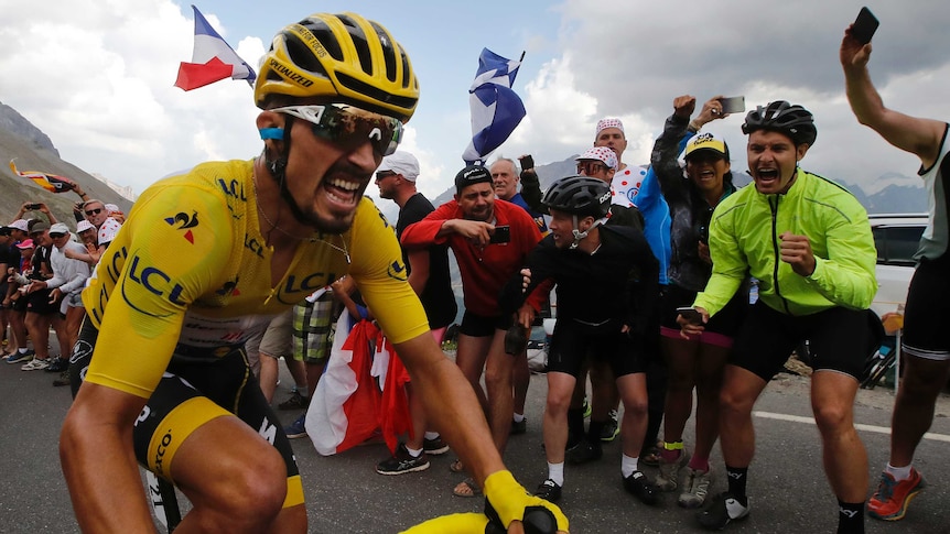 The race leader in the yellow jersey grimaces as crowds wave him on at the Tour de France.