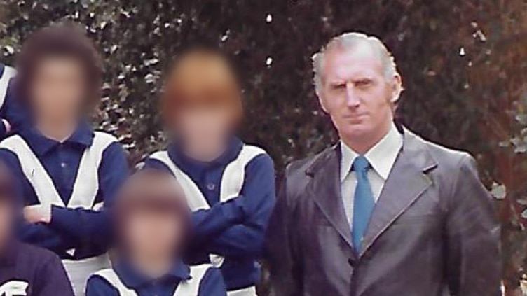 An old colour photo of a man posing with a football team of boys. The boys' faces are blurred.