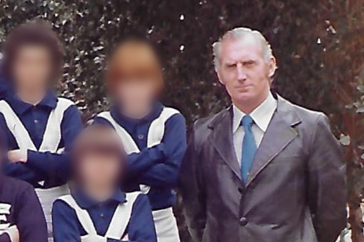 An old colour photo of a man posing with a football team of boys. The boys' faces are blurred.