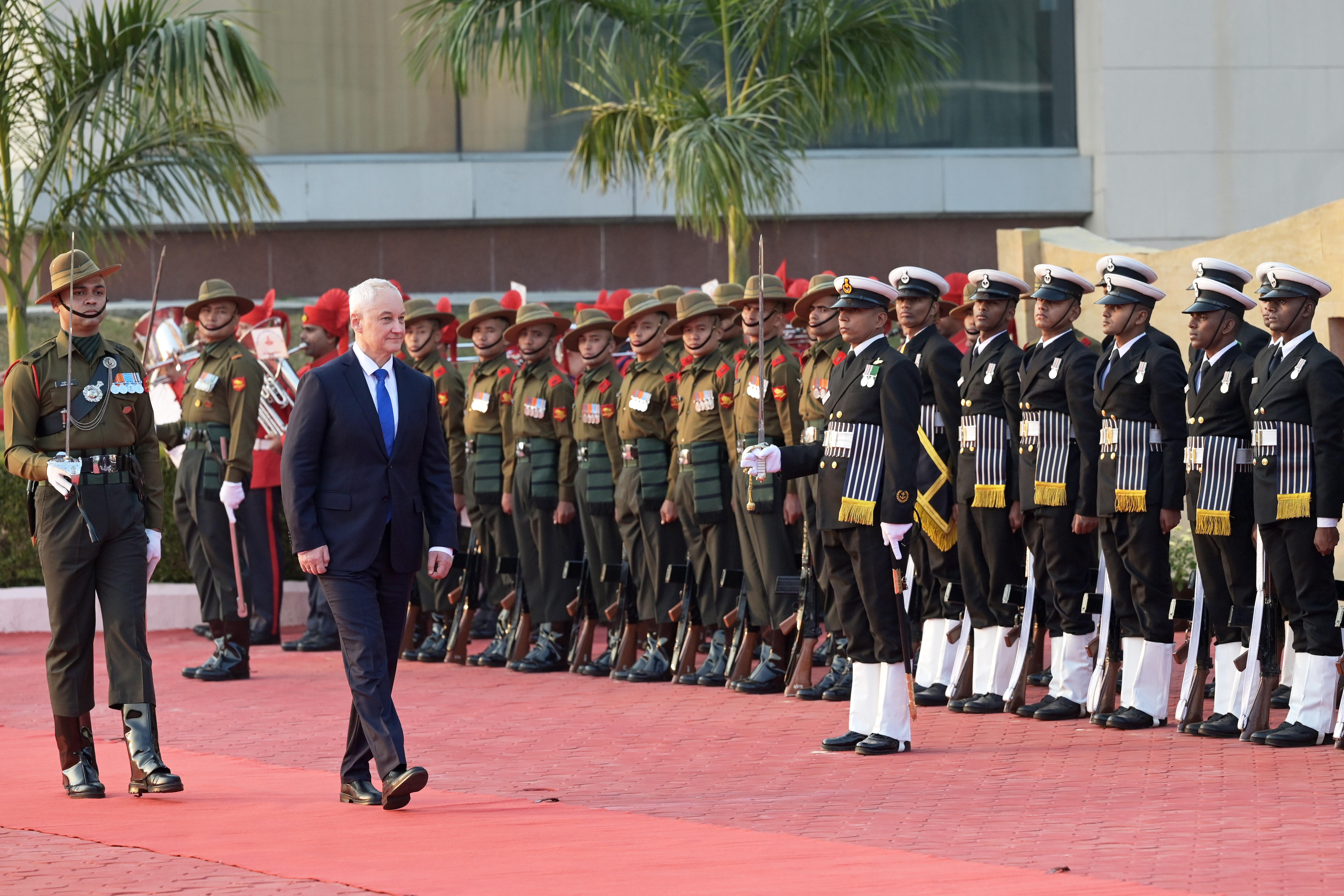 Un hombre de traje pasa junto a decenas de soldados con espléndidos uniformes en una alfombra roja.