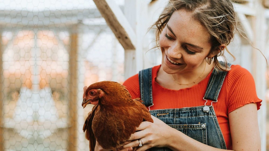 Woman in red shirt and overalls smiles while holding chicken for story about whether healthy, happy chickens are better for you