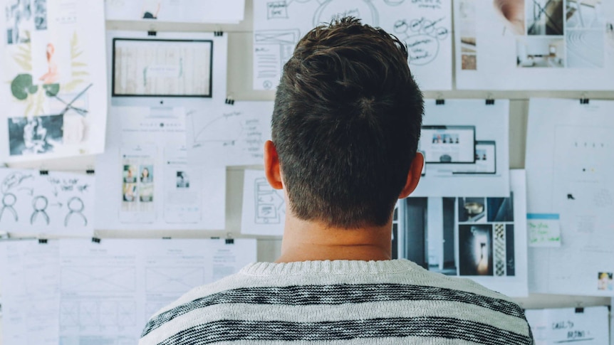 A man deep in thought, looking at a notice board.