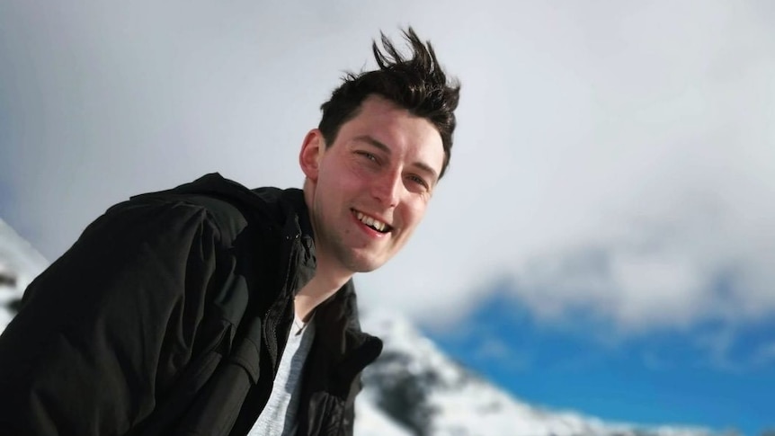 Mr Ness has dark hair and a dark jacket and is on a snowfield. He is smiling happily at the camera.