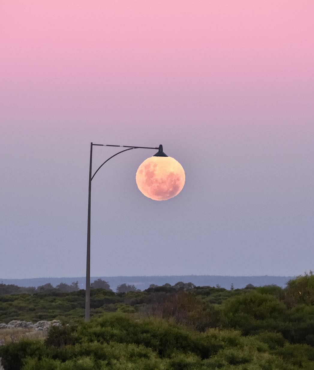 The full moon positioned under a street lamp.