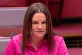 Senator Lambie wearing a bright pink shirt with a glare on her face in the Senate