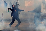 A masked protester throws a bottle as smoke and gas fills the air during clashes.