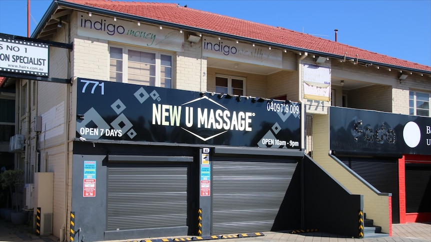 A photo of a sign reading New U Massage with two closed roller doors.
