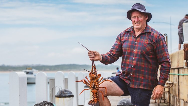 A man standing on a jetty holding a rock lobster. 