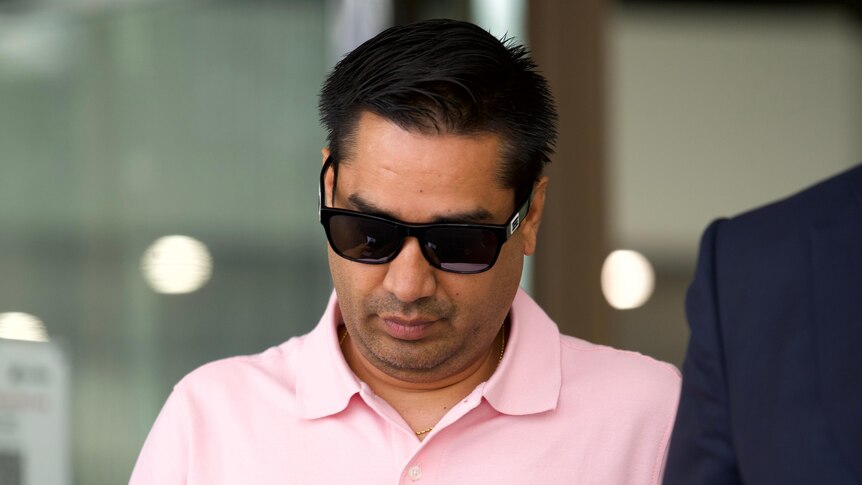 A man wears a pink polo shirt and sunglasses while leaving court