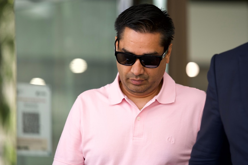 A man wears a pink polo shirt and sunglasses while leaving court