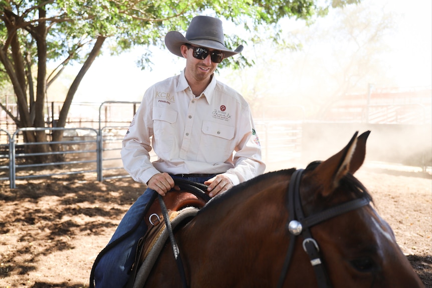 A man smiles at the camera. He is riding a horse.