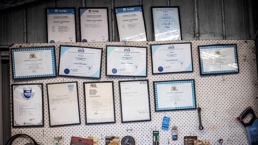 Thirteen framed TAFE certificates hang on a garage wall.