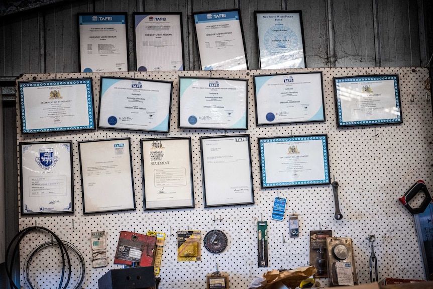 Thirteen frame TAFE certificates hang on a garage wall.