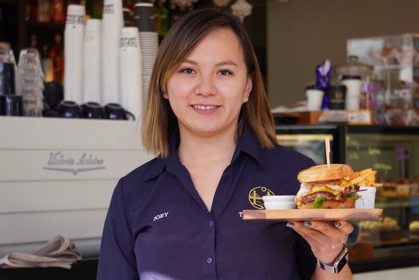 Joey Bui holding a wooden platter with a hamburger on it.