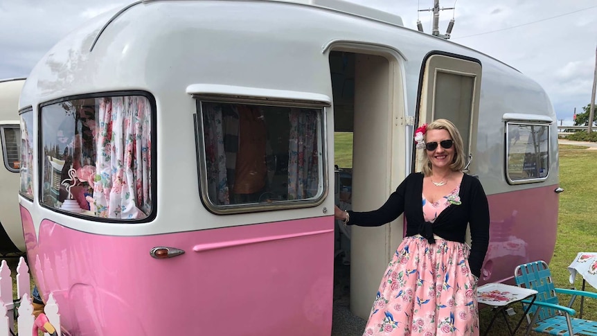 Monica is in pretty dress standing outside her Sunliner caravan at the 60th anniversary celebration in Forster