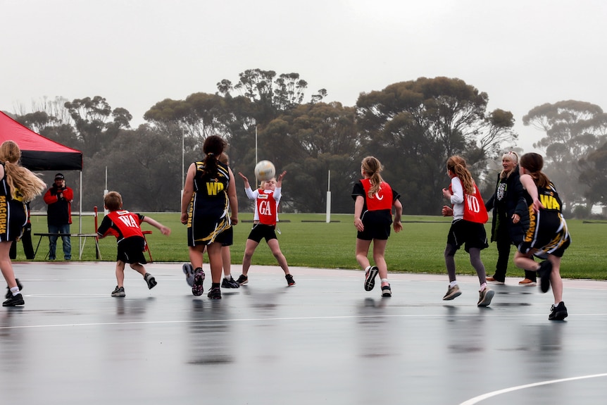 Children playing netball on an outside court wearing bright coloured uniforms