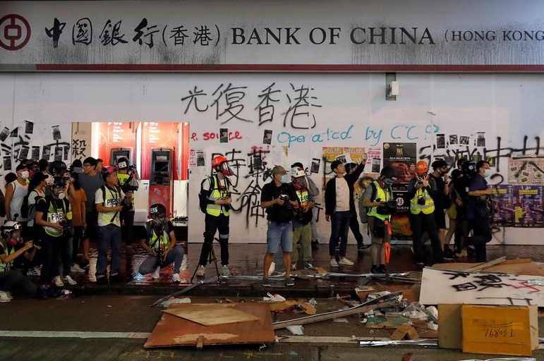 记者们站在中国银行一家分行外，这家银行在此次反政府抗议期间遭抗议者破坏。