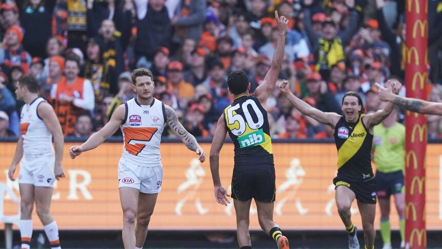 Marlion Pickett, in a  black singlet with 50 on the back, runs away with his hand up as a Richmond teammate runs towards him.