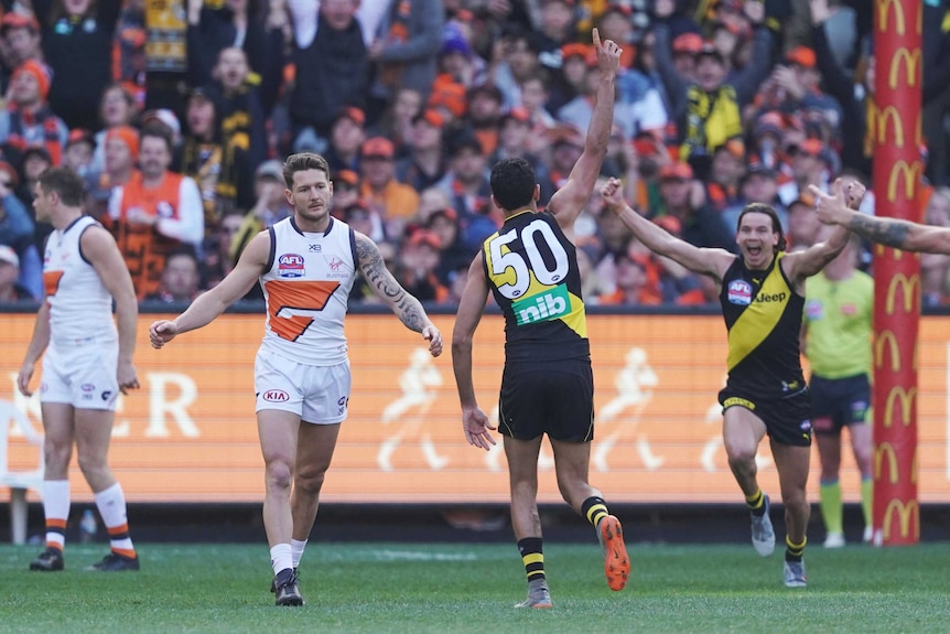 Marlion Pickett, in a  black singlet with 50 on the back, runs away with his hand up as a Richmond teammate runs towards him