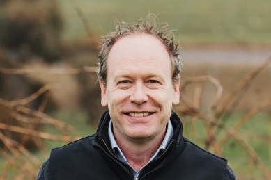 A close-up of a smiling man, receding hairline, background blurred.