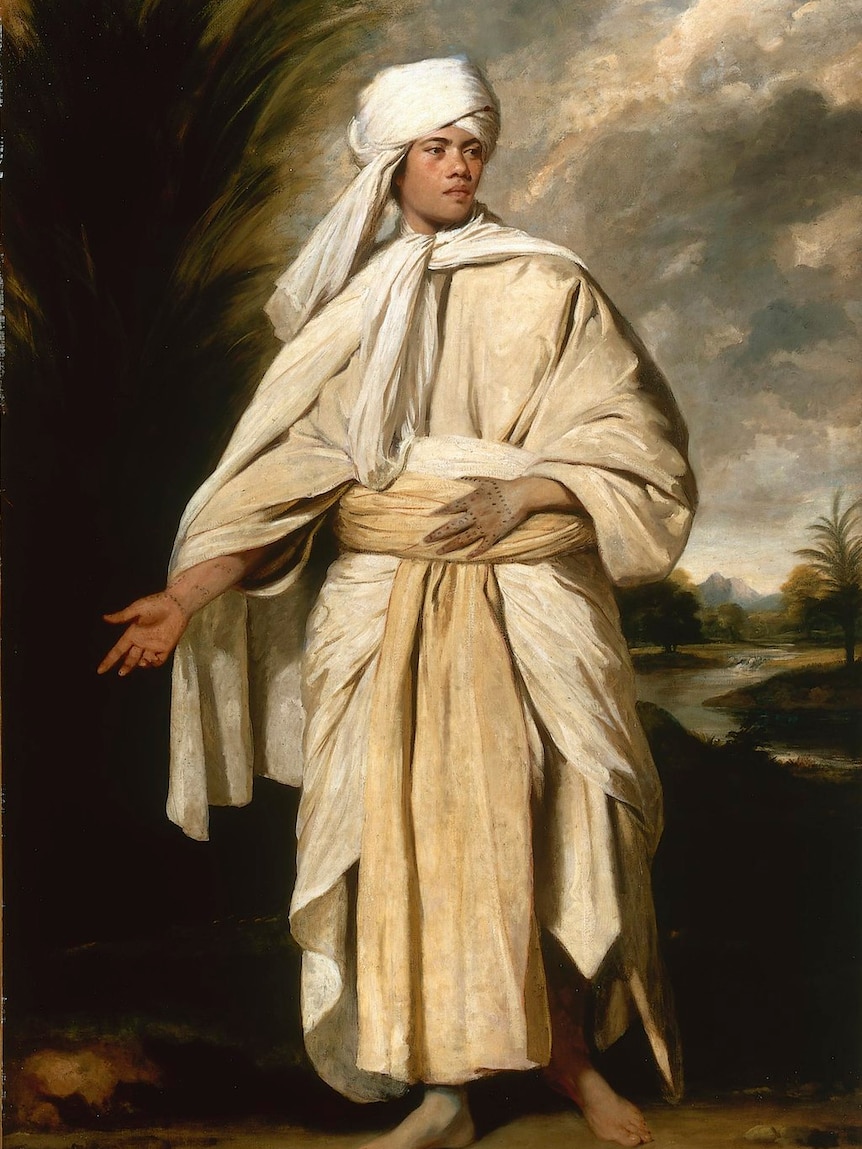 Portrait of a Tahitian man who is covered up in long white robes, but traditional tattoos can be seen on his hands