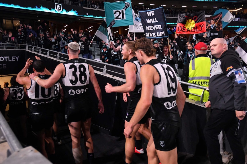 As Port Adelaide players walk off the field, a large crowd of fans cheer and hold flags and banners