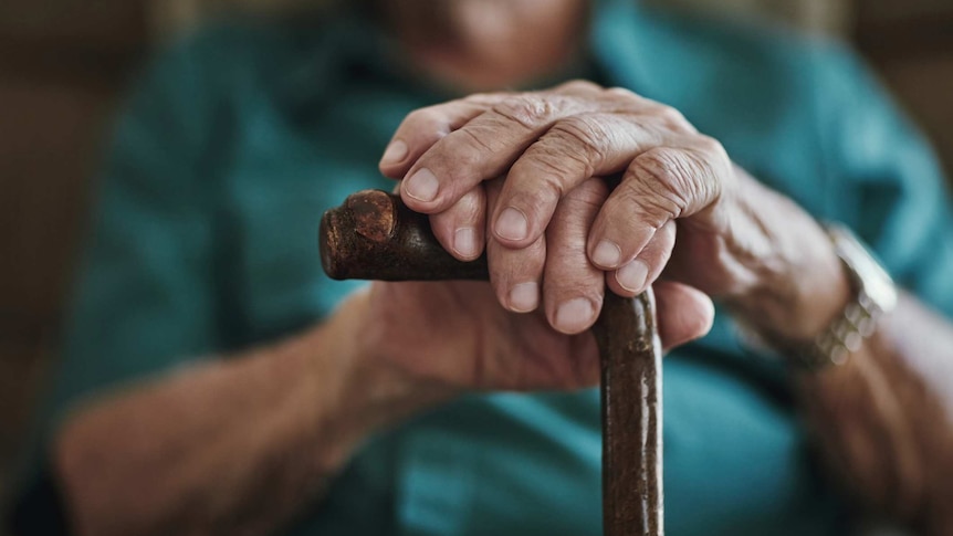 Cropped shot of an unrecognisable elderly man with his two hands leaning on walking stick.