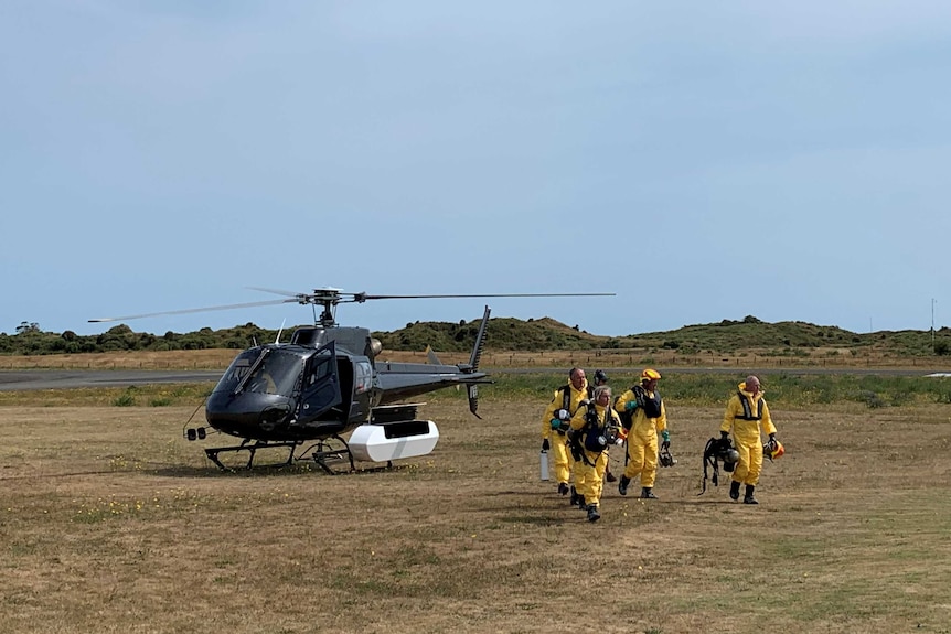 A group of people in yellow suits walk away from a landed helicopter.