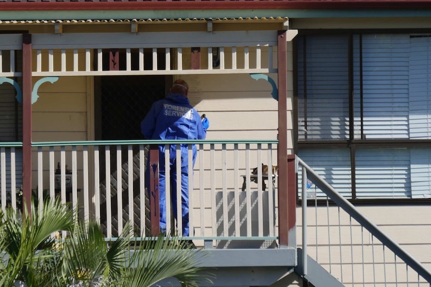 A police officer uses forensic instruments near the front door of a house.